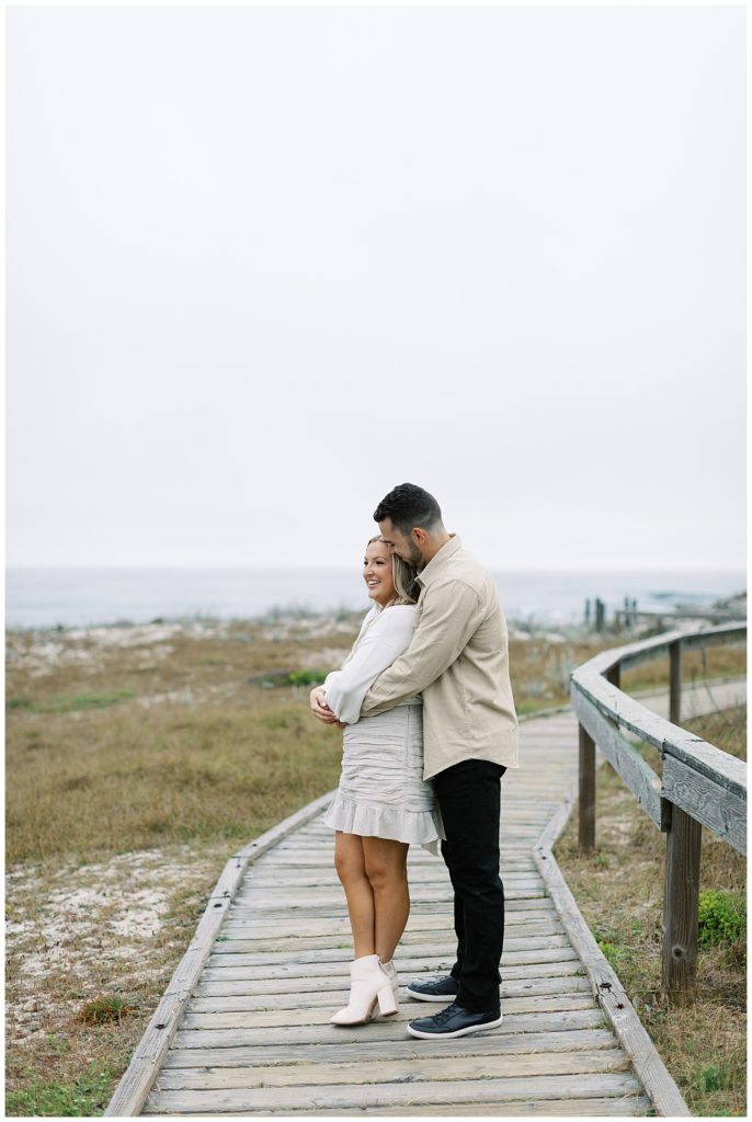 couple in each other's arms on a wooden walkway overlooking Spanish Bay