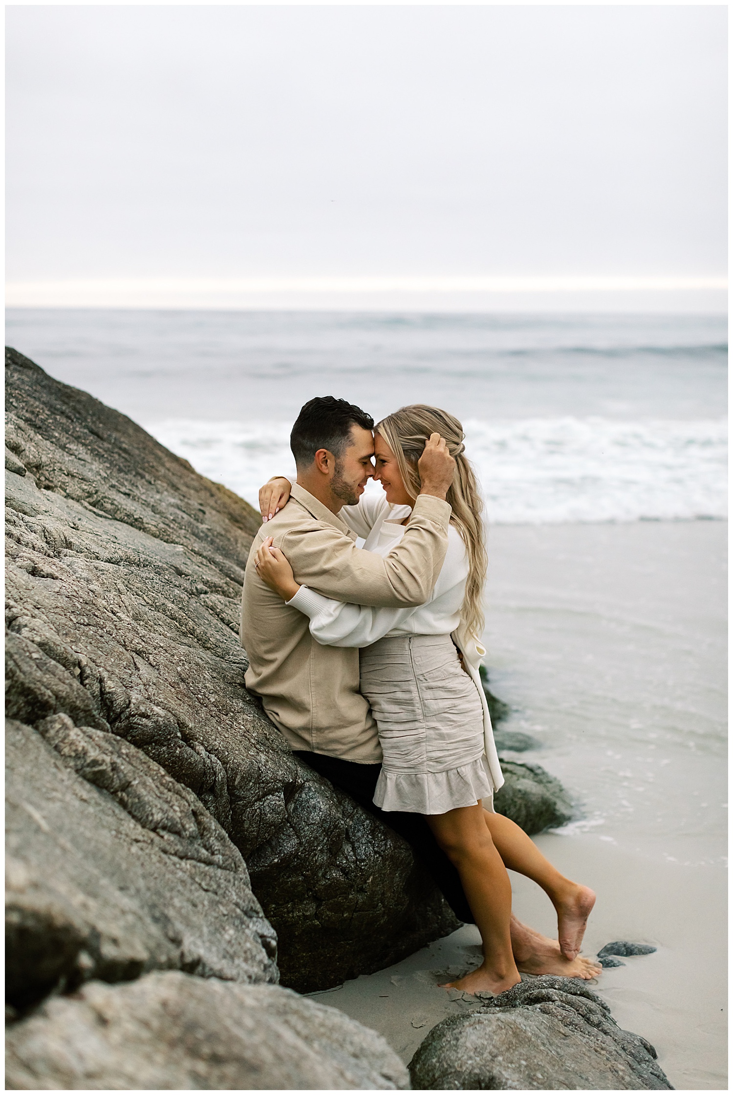 portrait of the couple embracing and touching their foreheads together while sitting on the rocks