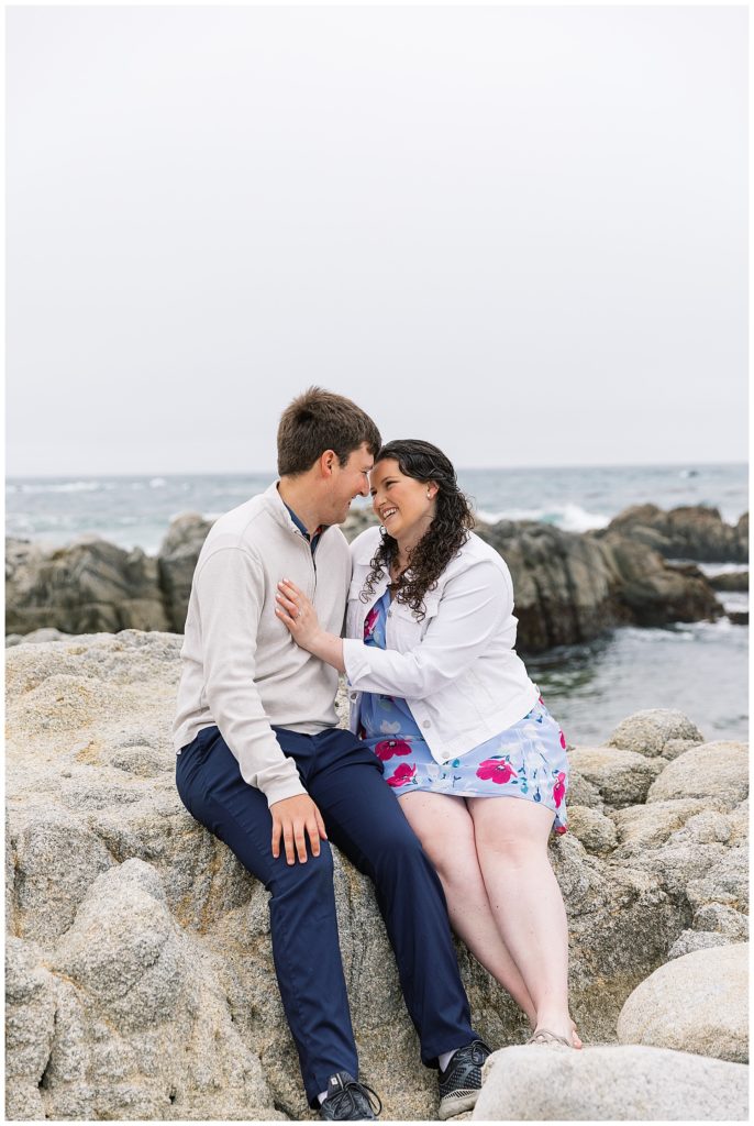 portrait of the couple sitting together on the rocks at Spanish Bay after their surprise proposal