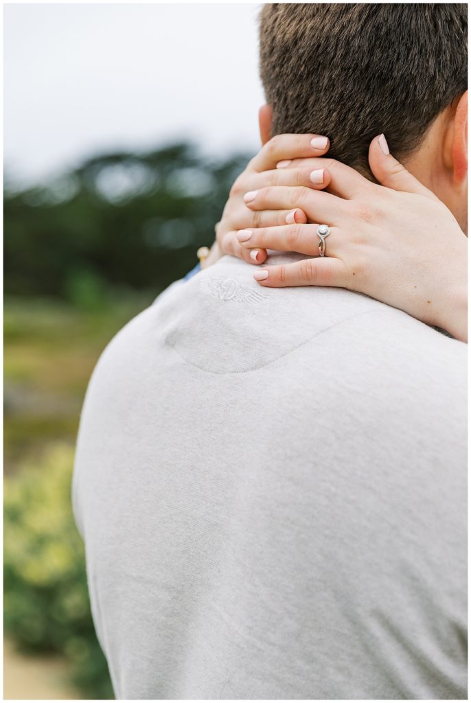 woman's hands showing her engagement ring around her fiancé's shoulders
