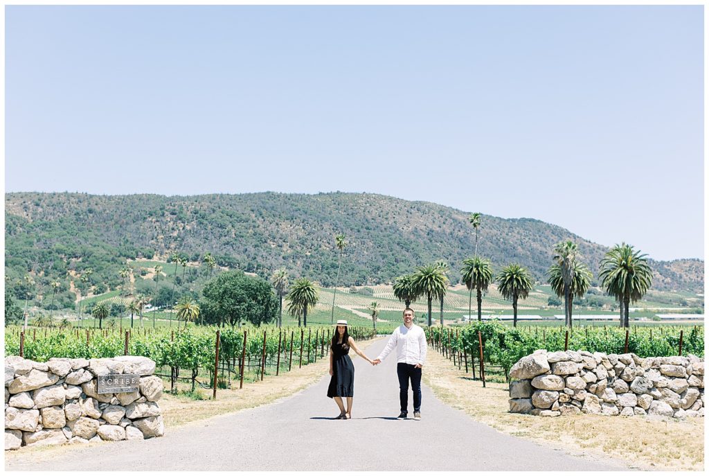 photograph of couple in front of Scribe Winery in Sonoma surrounded by vineyards, stone walls and palm trees by film photographer AGS Photo Art