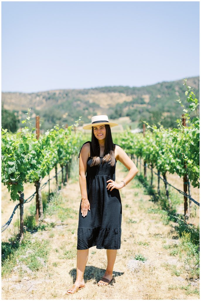 portrait of the soon-to-be-a-bride wearing a hat and black dress in the vineyards