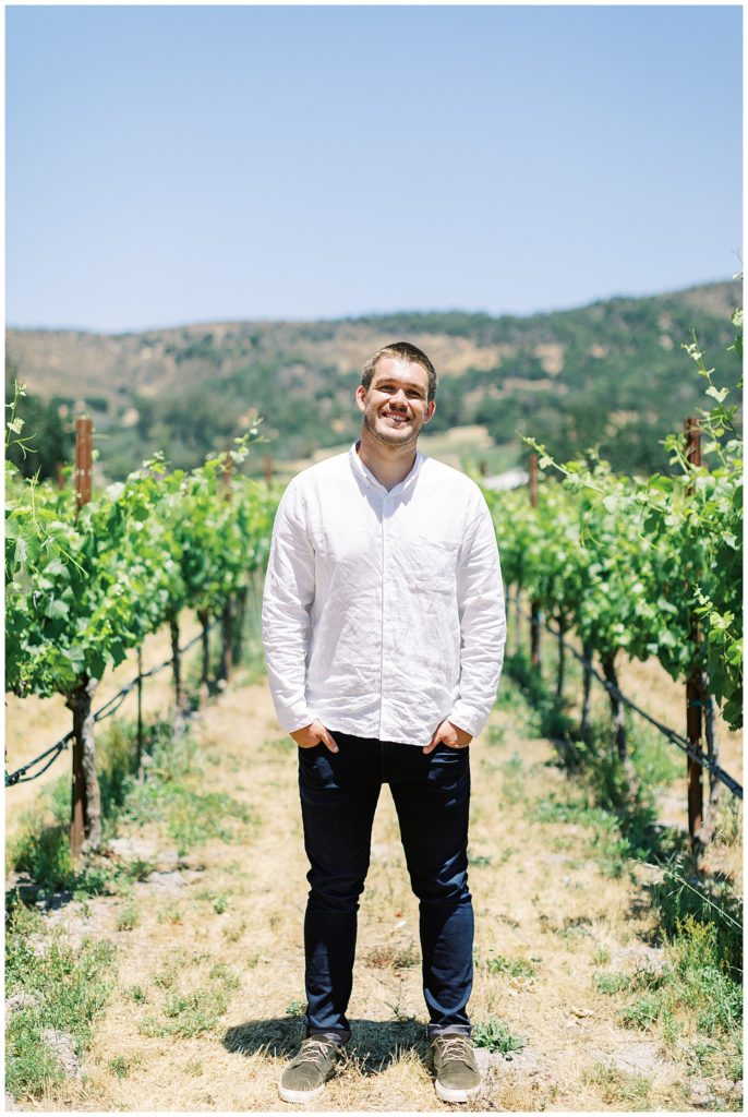 portrait of the soon-to-be-a-groom wearing a white button up and jeans in the vineyards