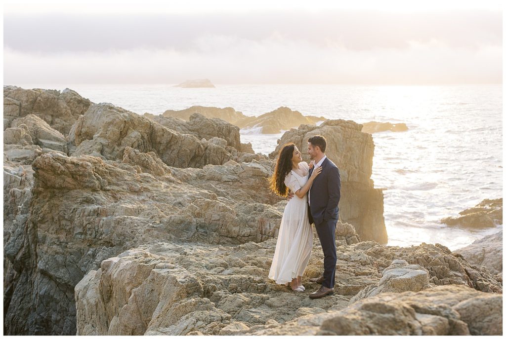 couple on the rocks with waves crashing behind them for their Big Sur Engagement + Bernardus Wedding by film photographer AGS Photo Art