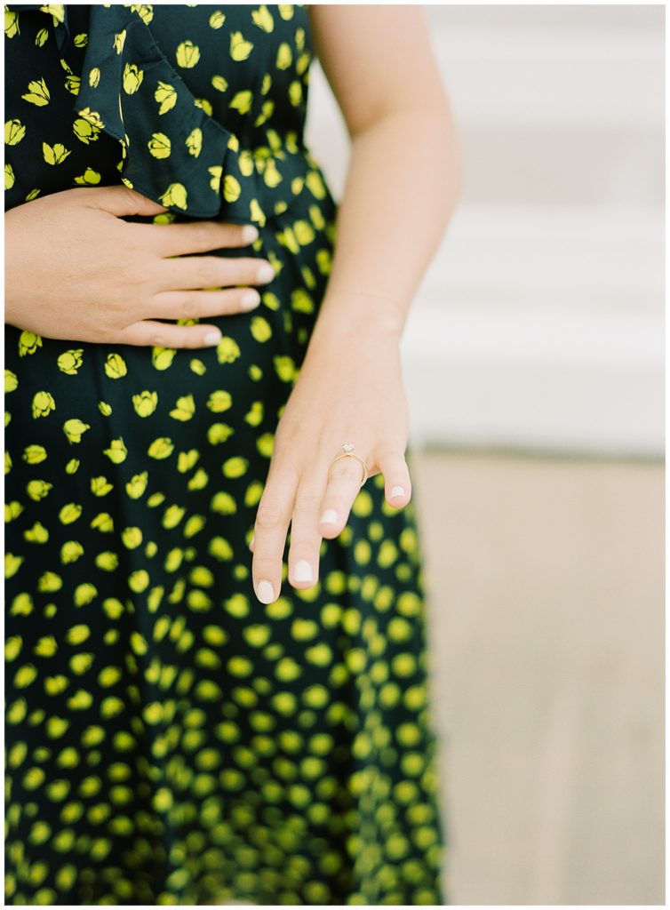 woman in a black dress with yellow flowers looking down at her engagement ring on her finger