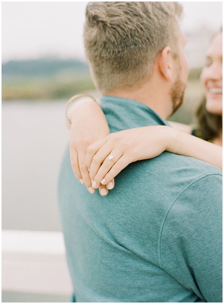 woman's arms over her fiancé's shoulders with a focus on her new engagement ring
