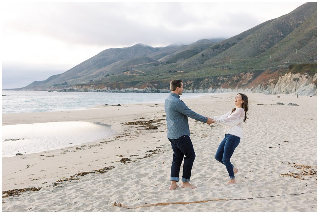 couple hand in hand and dancing on the sand during their engagement session in Big Sur by film photographer AGS Photo Art
