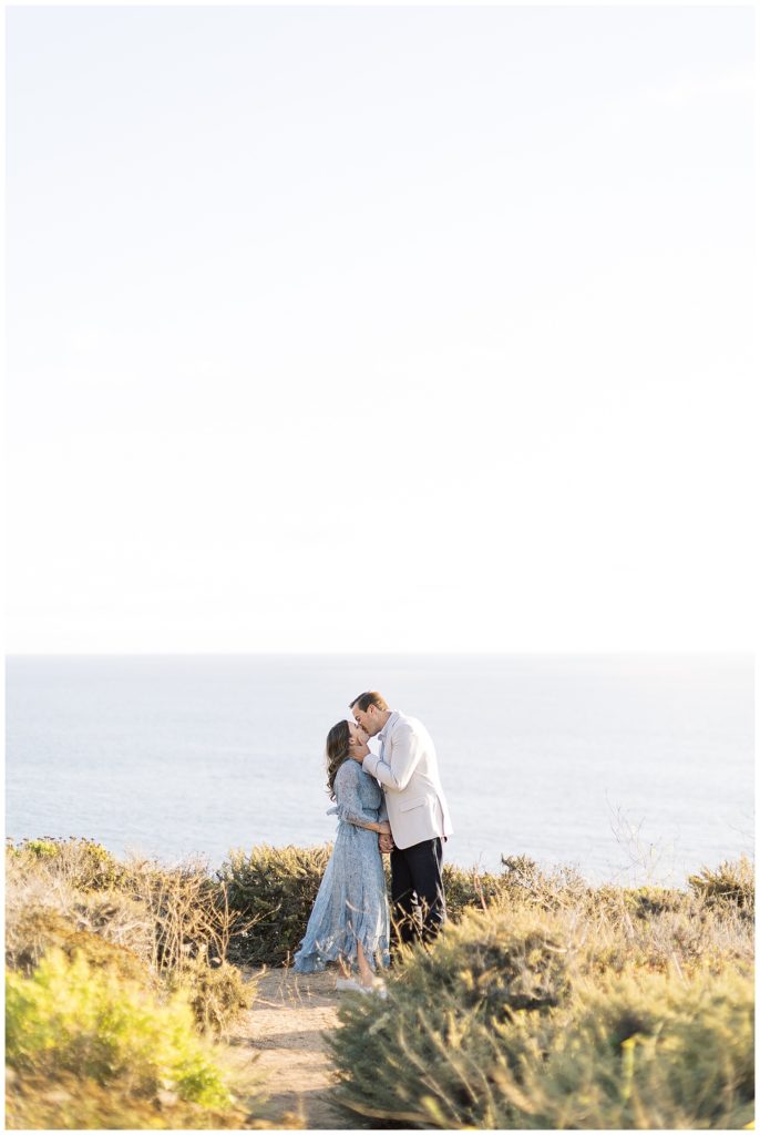 couple sharing a kiss surrounded by greenery with the ocean behind them