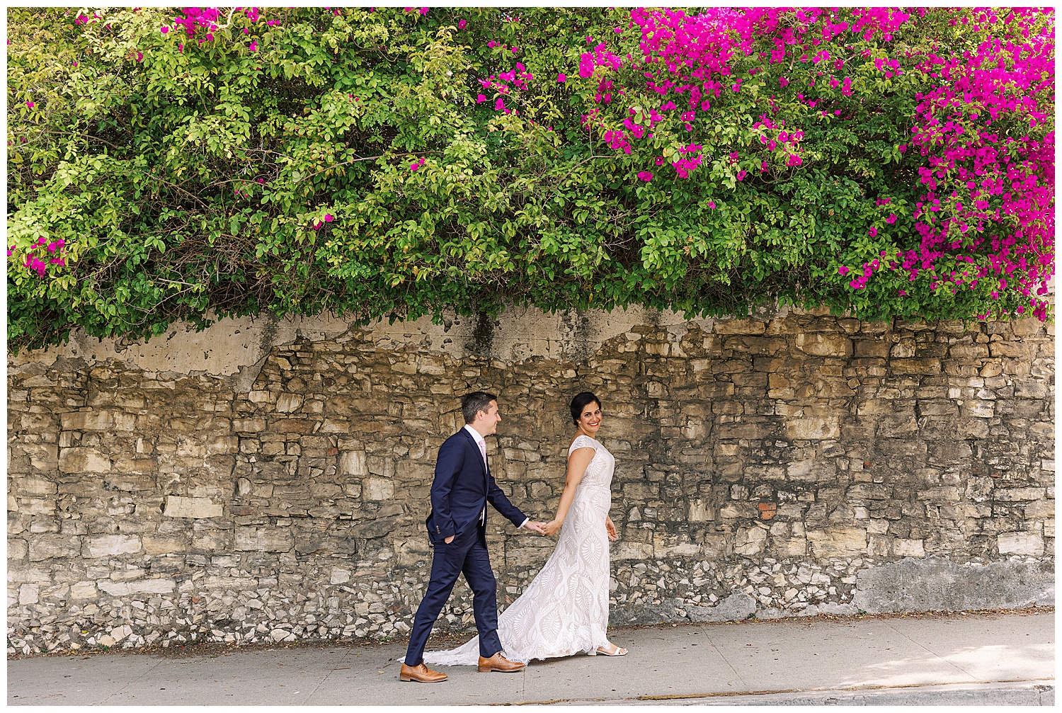 bride and groom walking hand in hand up the sidewalk at The Perry House with pink flowers hanging overhead