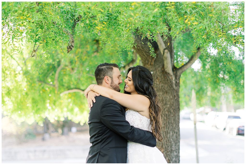 couple embracing and smiling at each other with a large green tree behind them during their Classic Monterey Bay Wedding
