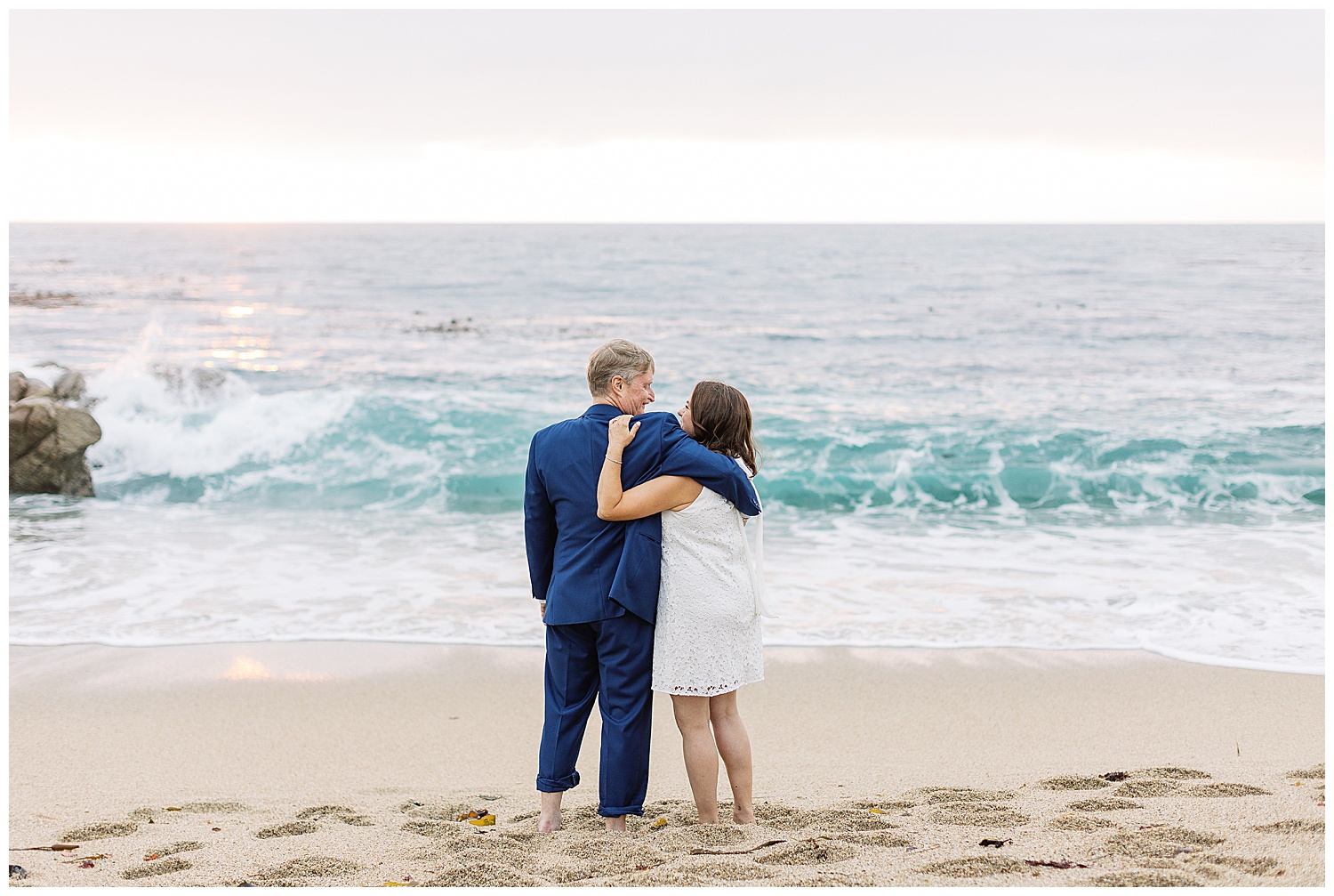 bride and groom with their backs to the camera as they smile at each other on the shoreline