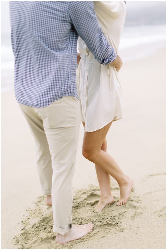 photo of the couple from the shoulders down embracing at the beach with their feet in the sand