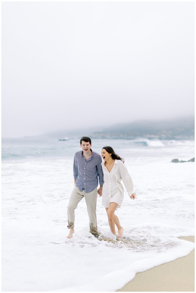 couple romping in the water at the beach during their Big Sur engagement shoot