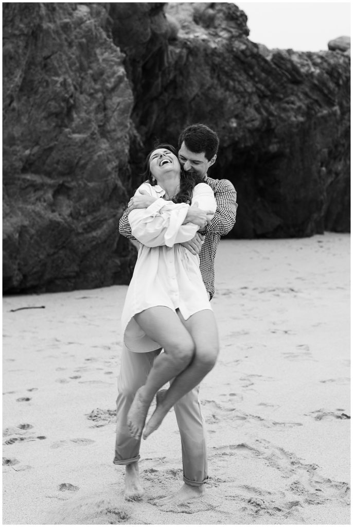 black and white Big Sur engagement shoot portrait of the couple spinning happily at the beach