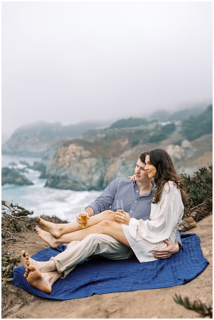 couple enjoying champagne on a blue blanket overlooking the Big Sur coastline