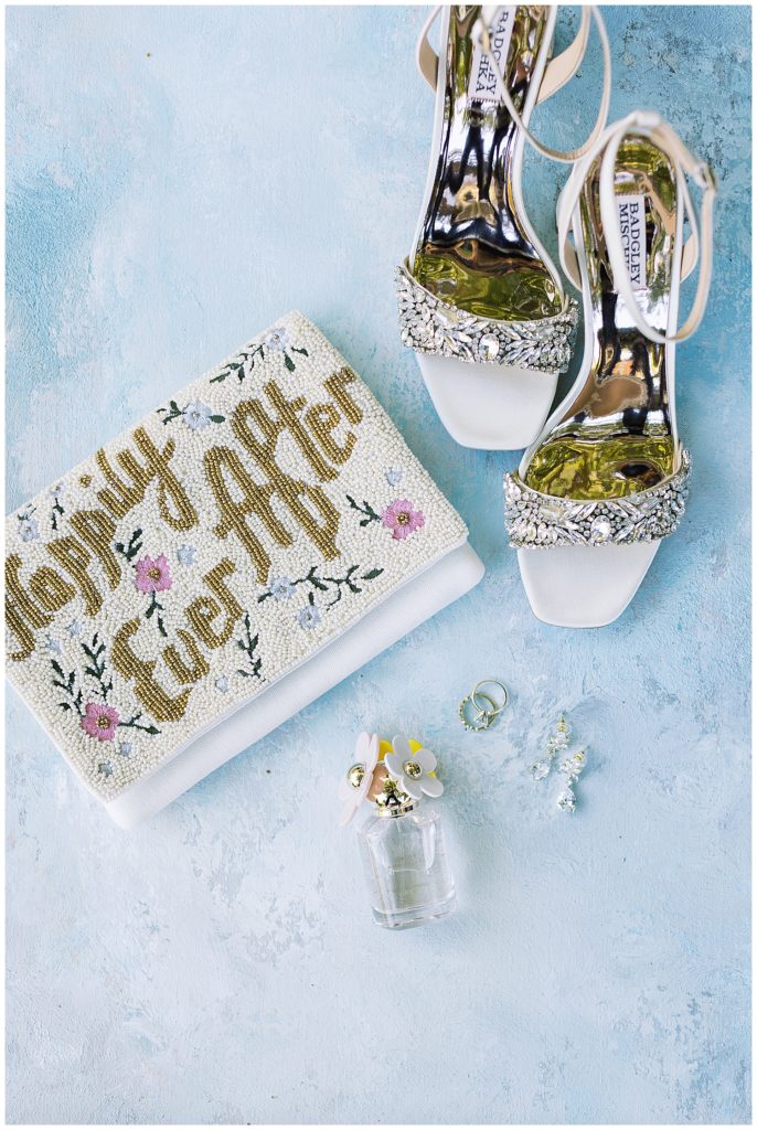 bridal details including her clutch reading "Happily Ever After", her Badgley Mischka heels, Daisy by Marc Jacobs perume, her wedding ring, and her earrings
