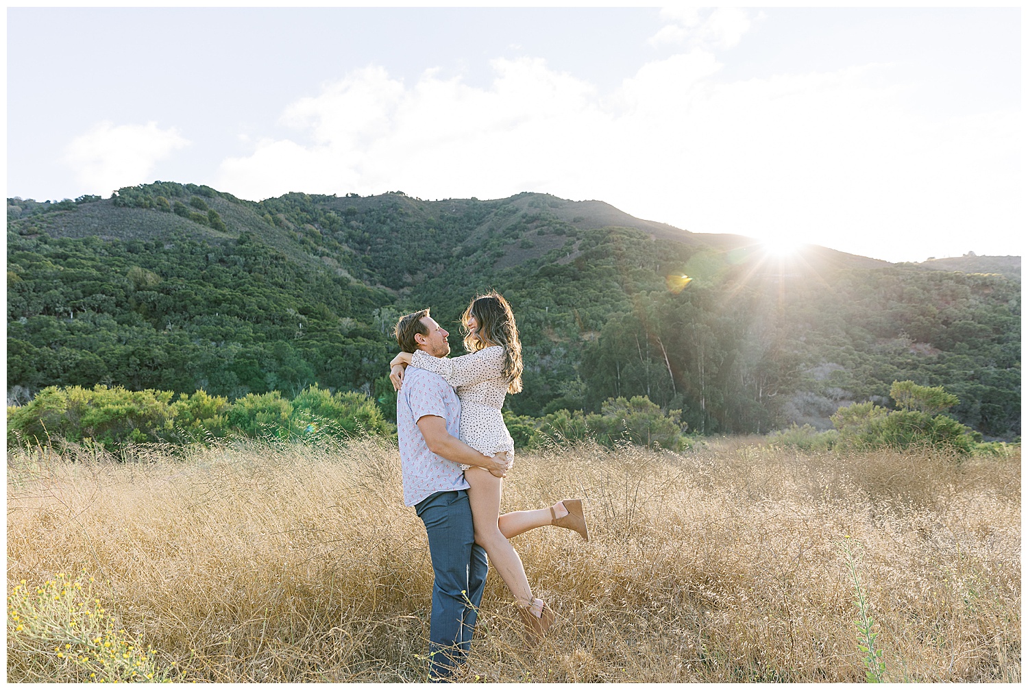 Carmel Valley engagement session portrait of a soon-to-be-groom holding up his fiancée in his arms as they smile with the sun peeking over the mountain behind them by film photographer AGS Photo Art