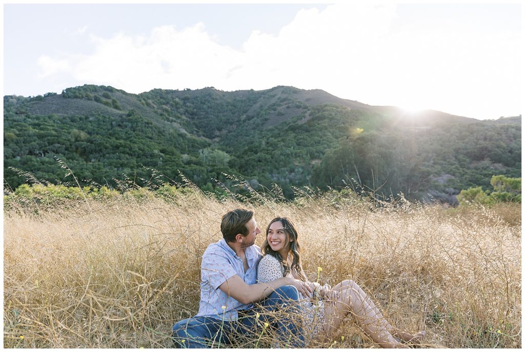 couple laying in the grass and smiling at each other during their Carmel Valley engagement session by film photographer AGS Photo Art
