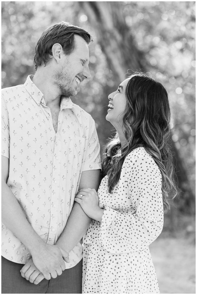 black and white Carmel Valley engagement session portrait of the couple smiling at each other under the trees