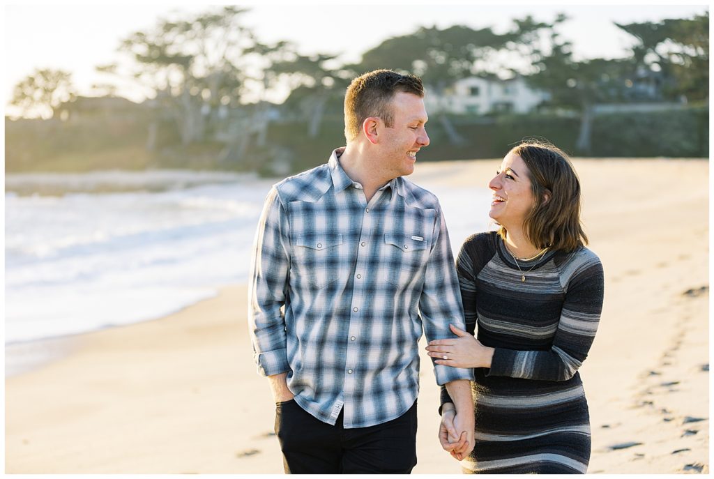 landscape photo of the couple walking down the beach and smiling at each other during their Carmel by the Sea engagement session