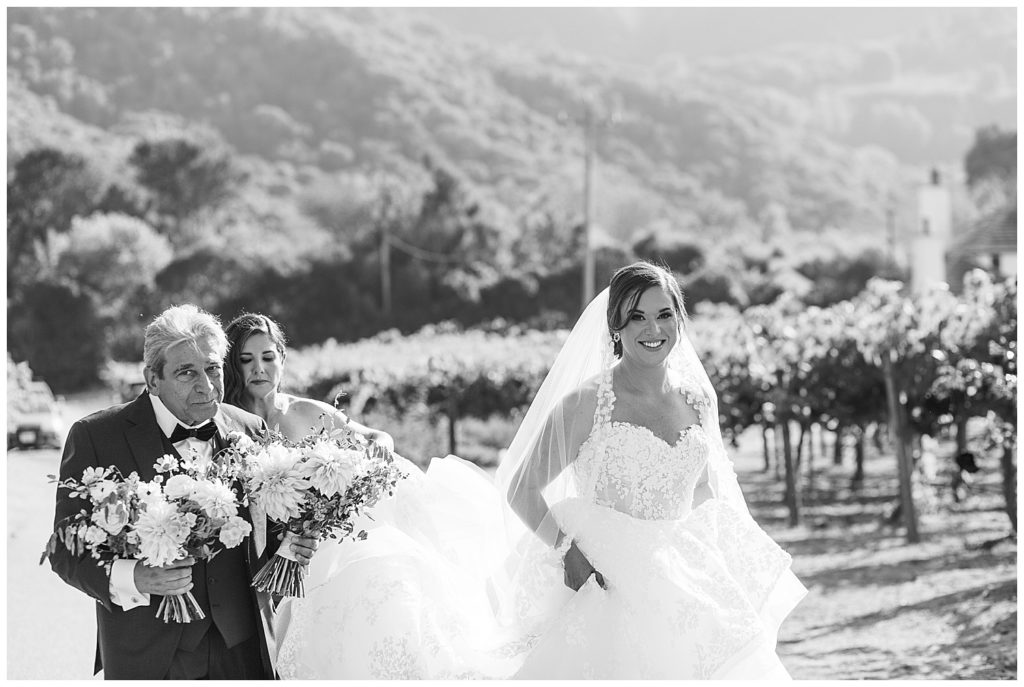 black and white Carmel by the Sea bridal portrait with the bride's father and maid of honor helping her down the aisle