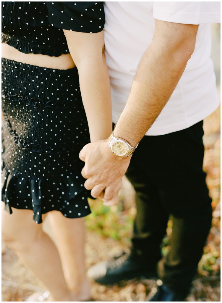 couple from the chest down hand in hand with a focus on the husband's gold watch