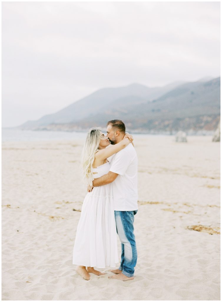couple in white sharing a kiss at the beach during their Big Sur anniversary session