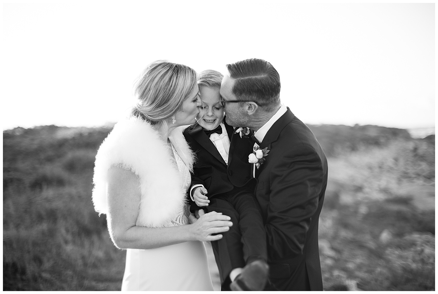 black and white photo of the bride and groom kissing their son on his cheeks by film photographer AGS Photo Art