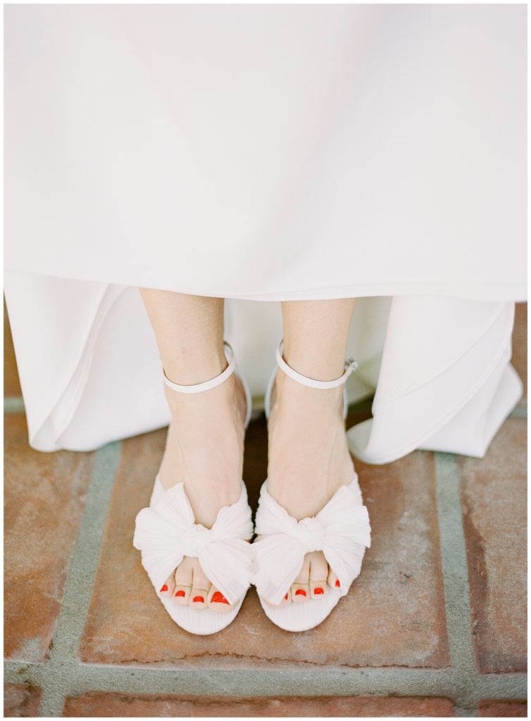 bride's Loeffler Randall heels with white bows and coral orange painted nails