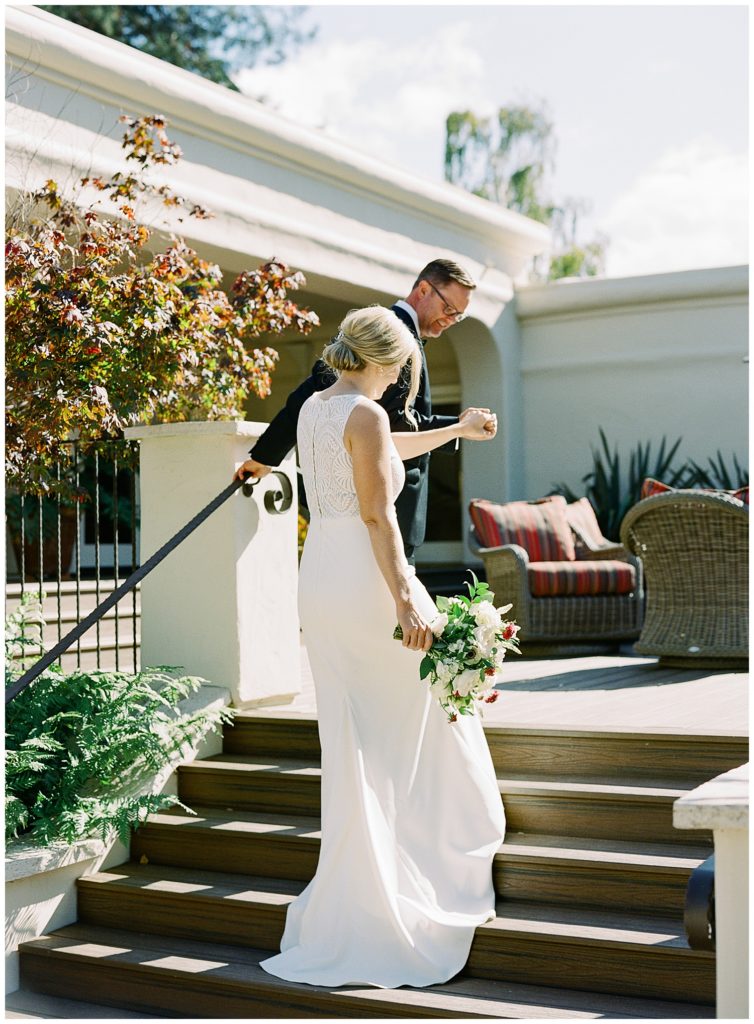 the groom leading his bride up the stairs and holding her hand while she holds her bouquet