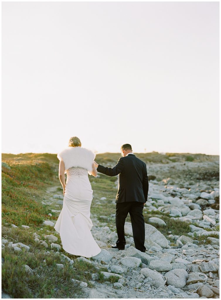 the bride wearing her fur coat as she and her groom adventure up the hill towards the setting sun at their MPCC Beach House intimate wedding