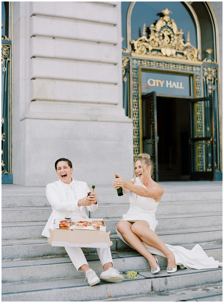 two brides celebrating their San Francisco City Hall Elopement on the steps with pizza and Moet champagne