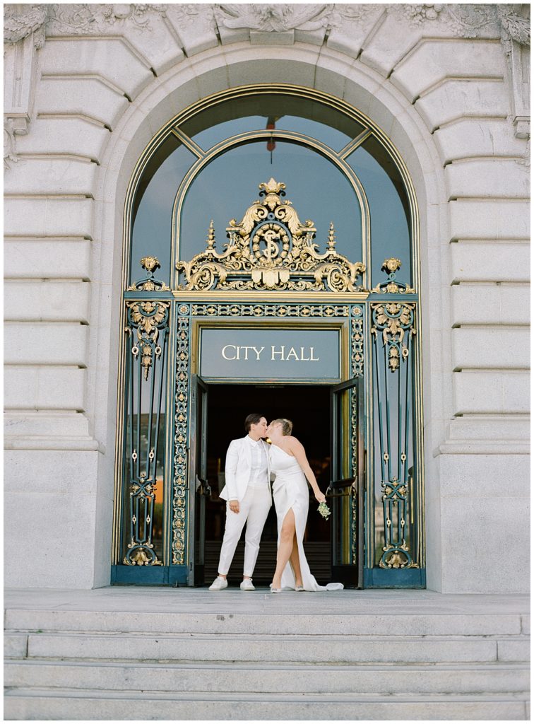 brides sharing a kiss at the entrance of San Francisco City Hall