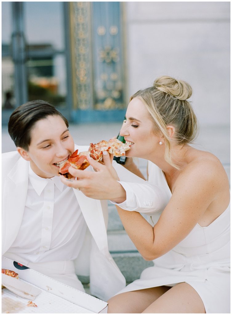 portrait of brides feeding each other pizza during their San Francisco City Hall elopement by film photographer AGS Photo Art