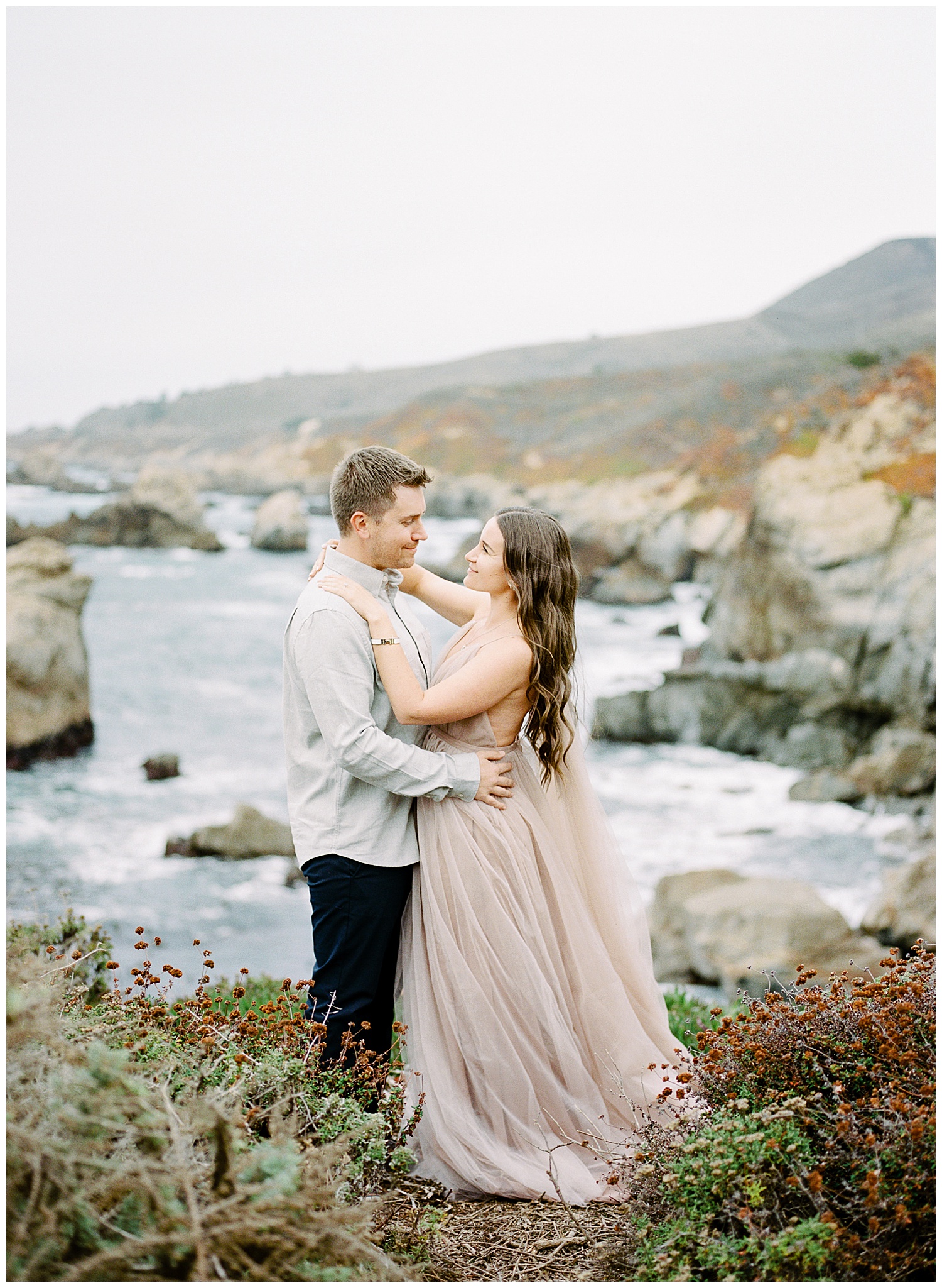 engagement photos in Big Sur with the couple gazing into each other's eyes and the coastline in the background