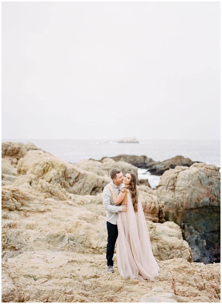 new bride's fiance kissing her cheek while she turns and smiles at the camera over her shoulder