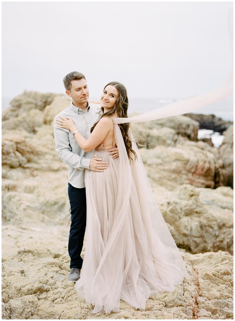 engagement photos in Big Sur featuring a pale blush dress with the sashes on its sleeves fluttering back