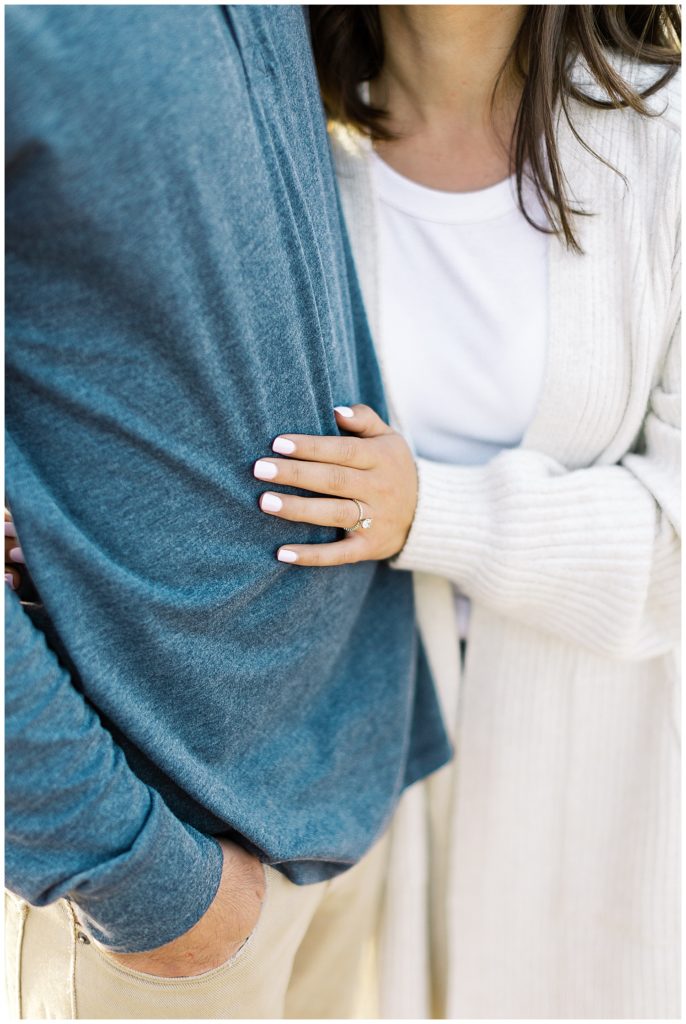 soft focus on woman's engagement ring as she hold's her fiancé's arm
