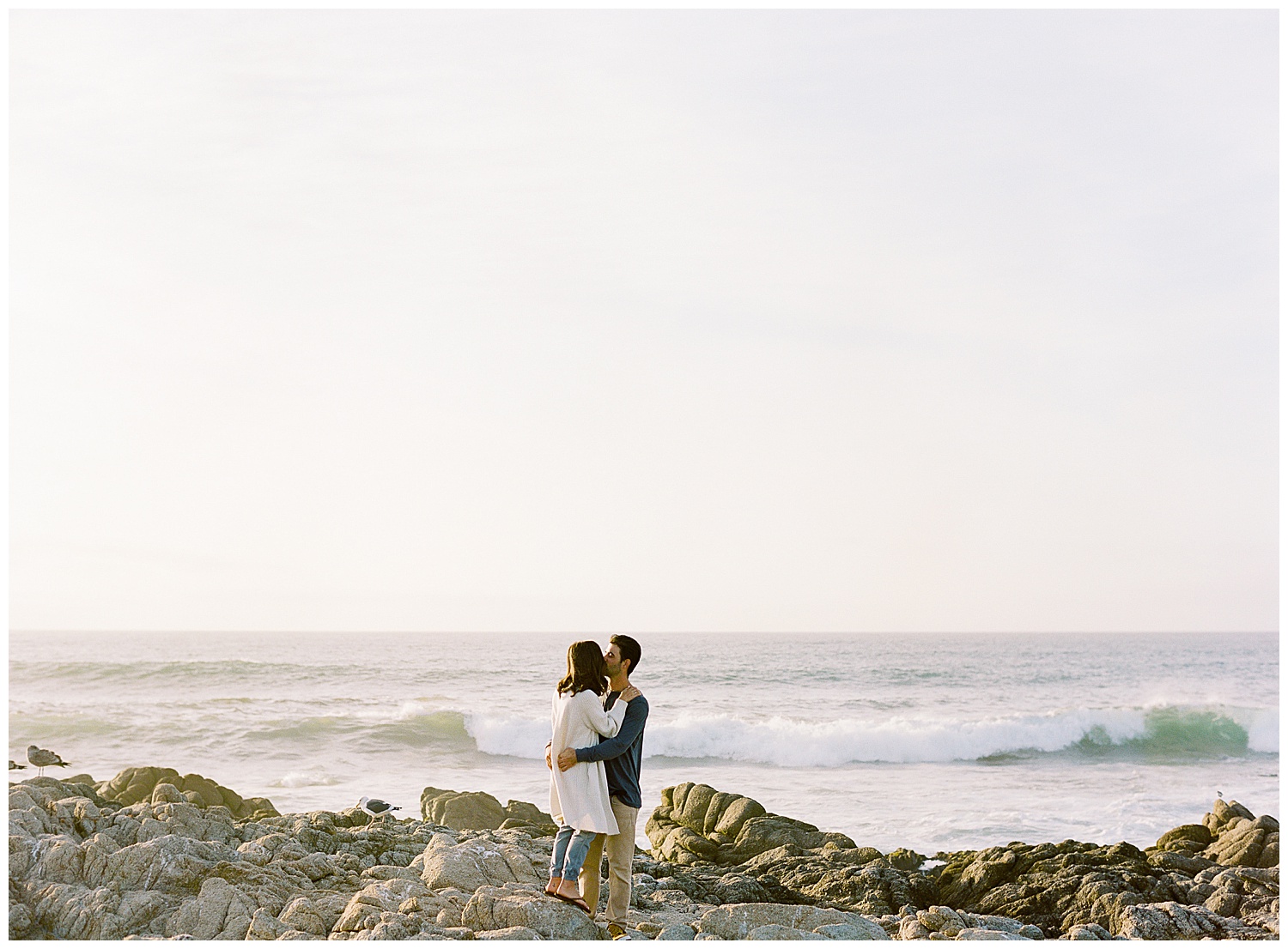 landscape engagement photo in Pebble Beach of the couple sharing a kiss with the waves crashing behind them