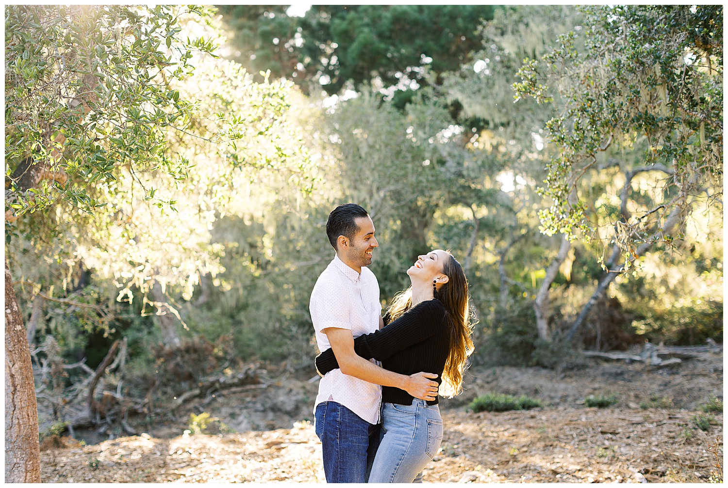 smiling couple in Del Monte Forest under the trees with light pouring in between the leaves and branches