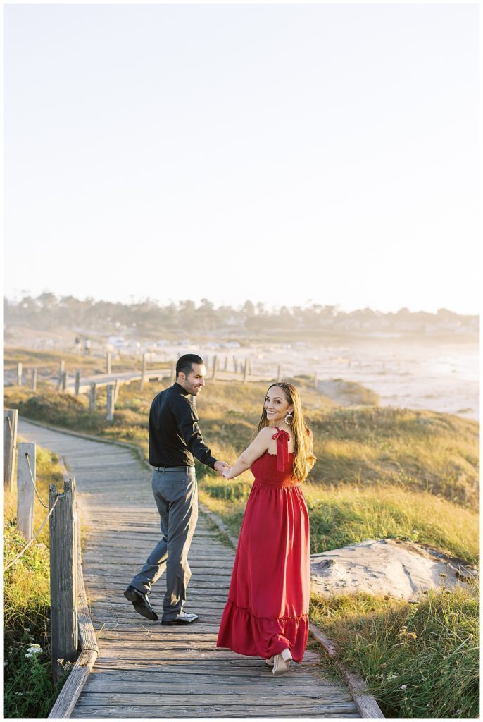 Pebble Beach engagement session on the coastline with the couple walking hand in hand away from the camera