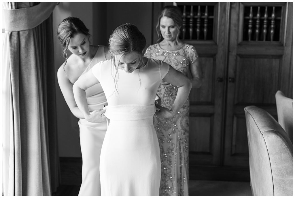 black and white getting ready photo of the bride being helped into her dress by her bridesmaid and mom