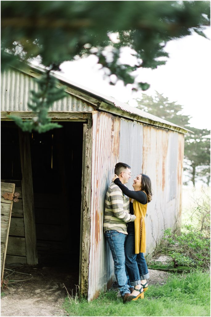 a couple leaning against a barn gazing into each other's eyes during Big Sur engagement photoshoot