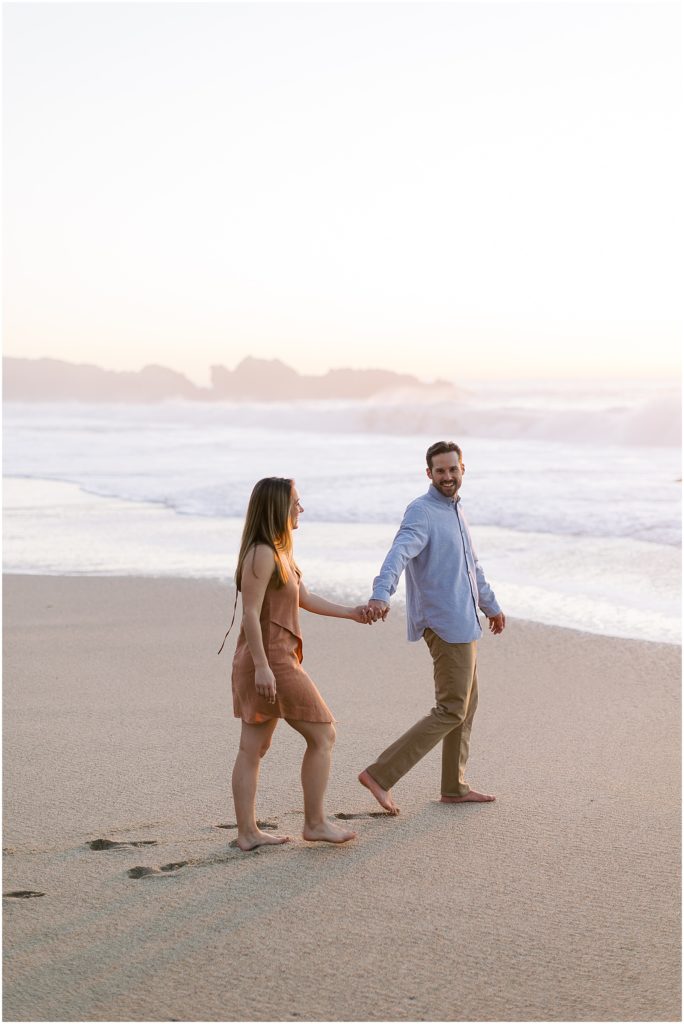 a couple holding hands and walking on the beach in Big Sur for their engagement photoshoot
