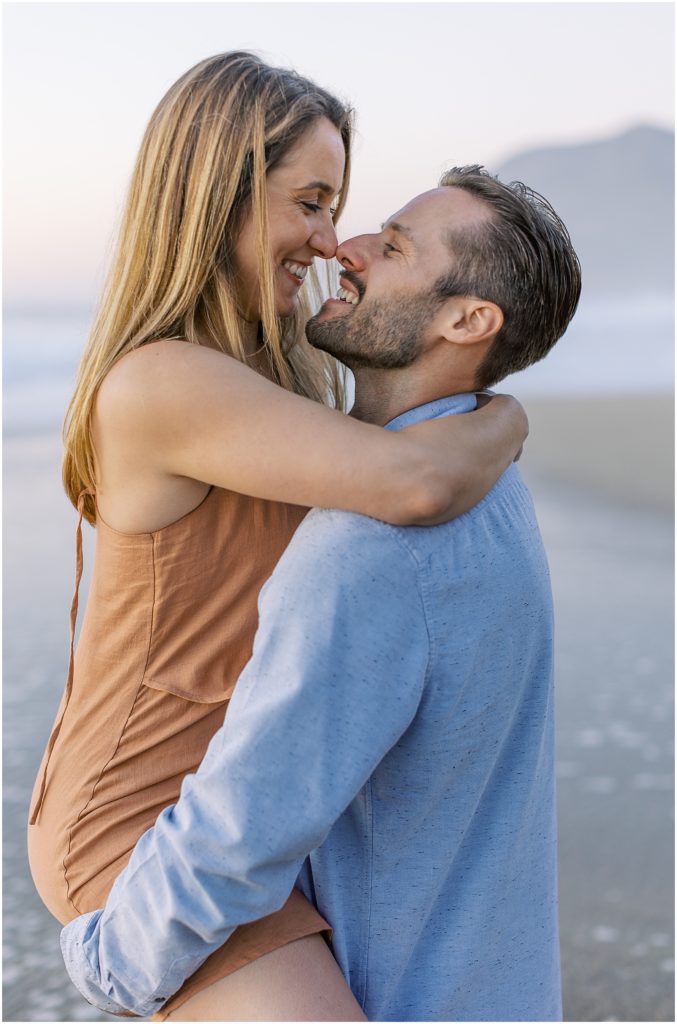 a man holding a woman and touching noses during Big Sur Engagement Photoshoot
