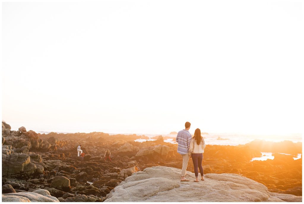 couple standing together on the rocks watching the sunset