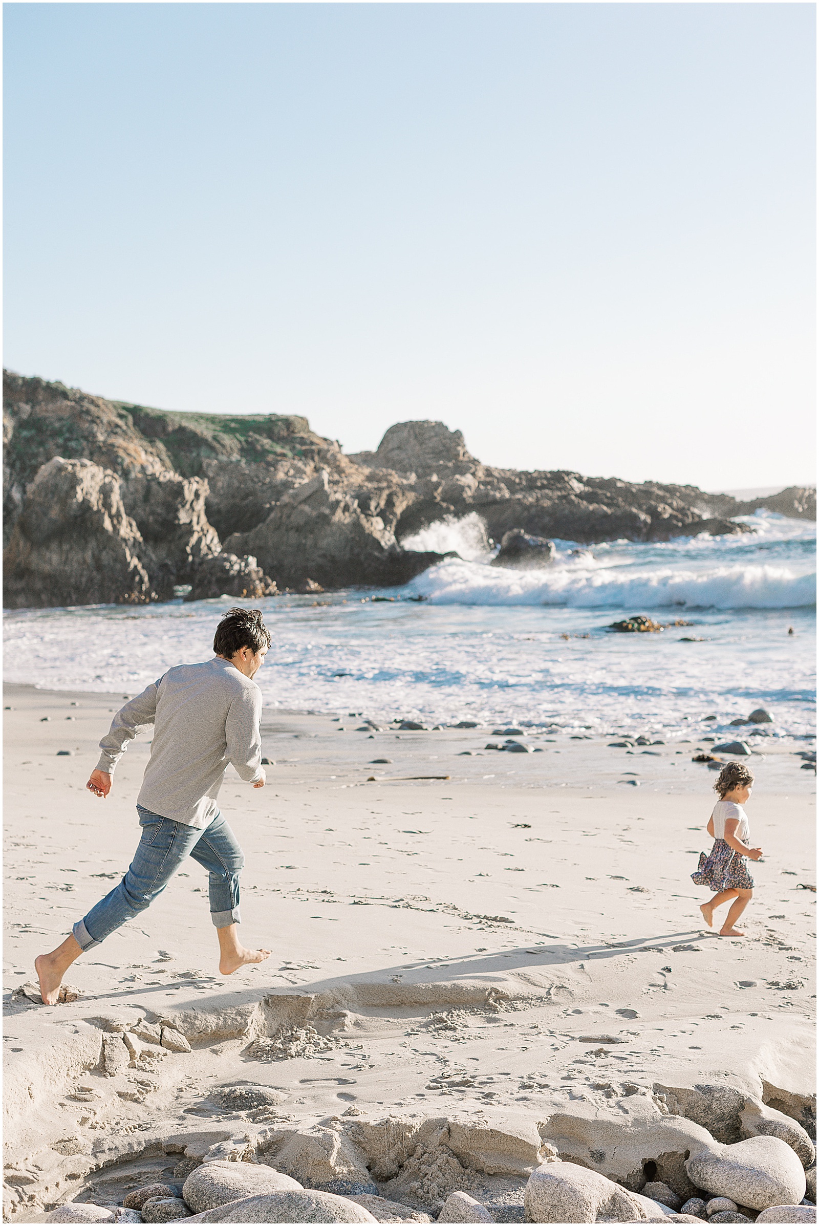a portrait of a father chasing his child along the beach