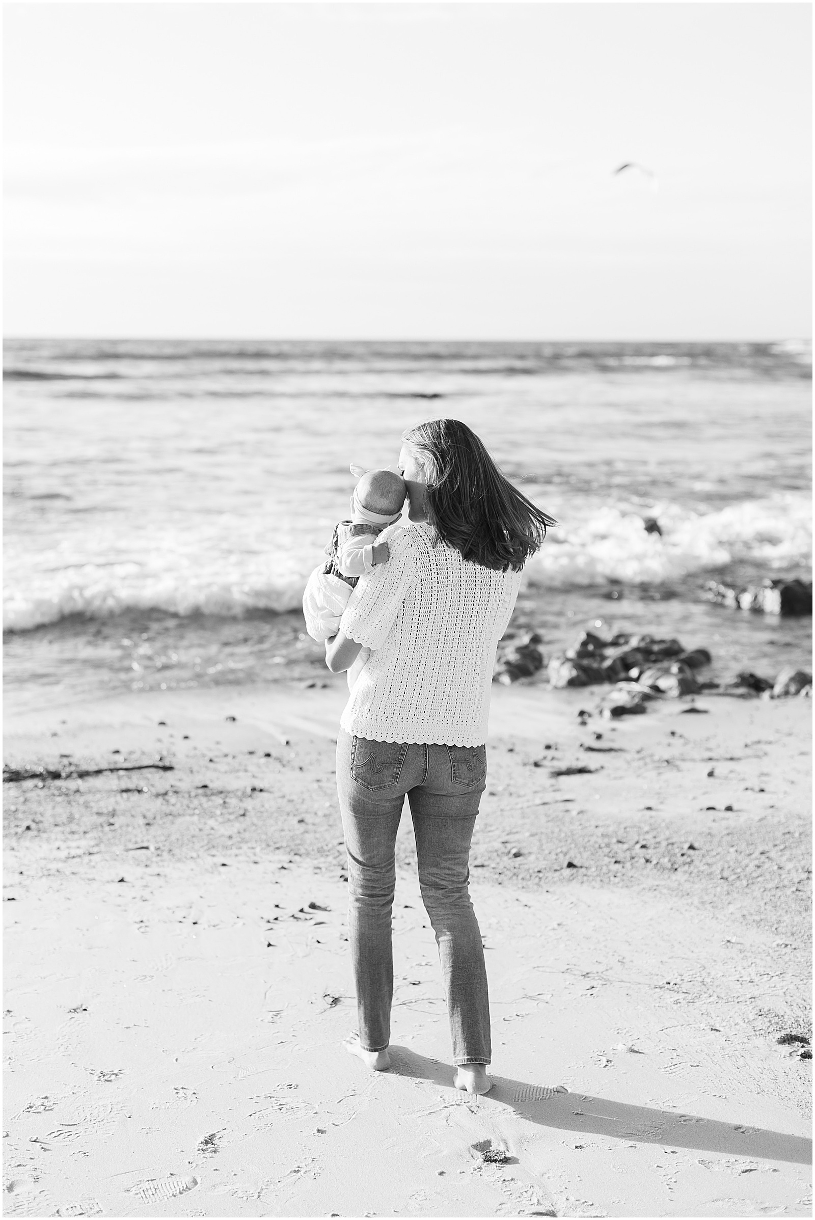black and white portrait of a mom carrying her baby near the ocean at Carmel Beach