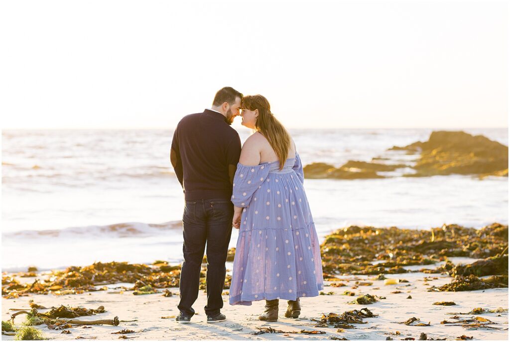 Photo of a man and woman embracing at the beach, with the sunsetting on the ocean behind them