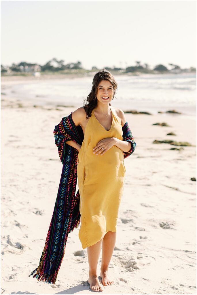 Pregnant woman wearing Mexican rebozo smiling and holding belly while being photographed by AGS Photo Art